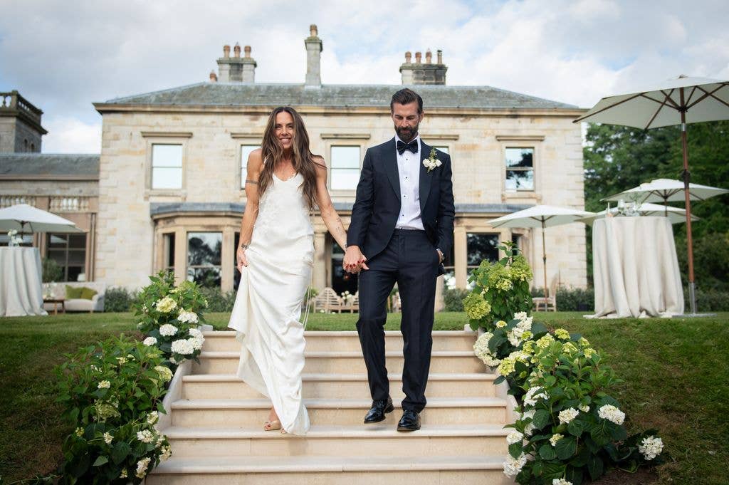 Melanie C and Chris Dingwall walk hand-in-hand down steps in front of a large house.