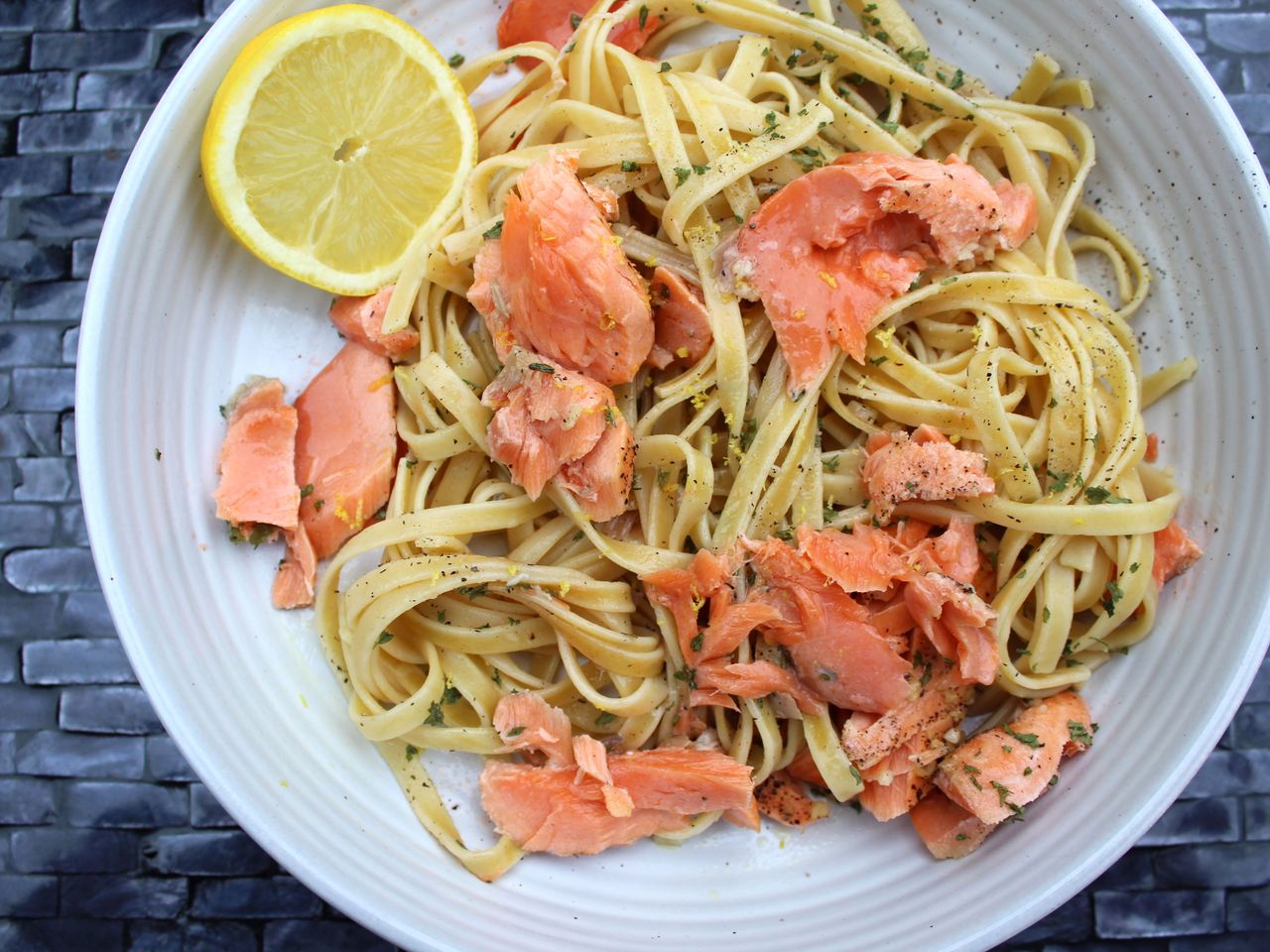 Fettuccini pasta topped with baked salmon and garnished with lemon slice