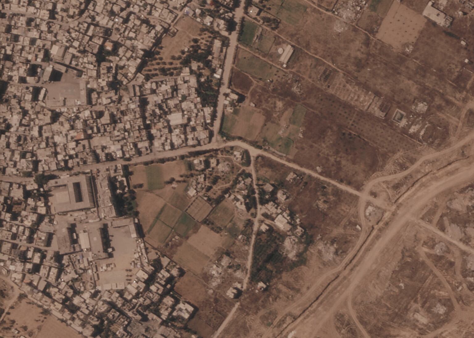 A section of an earth barrier being built by the Israeli military, right side of image moving top to bottom, in the central Gaza Strip. At left is the Maghazi refugee camp, and on the other side are homes demolished by the military (Planet Labs PBC via AP)