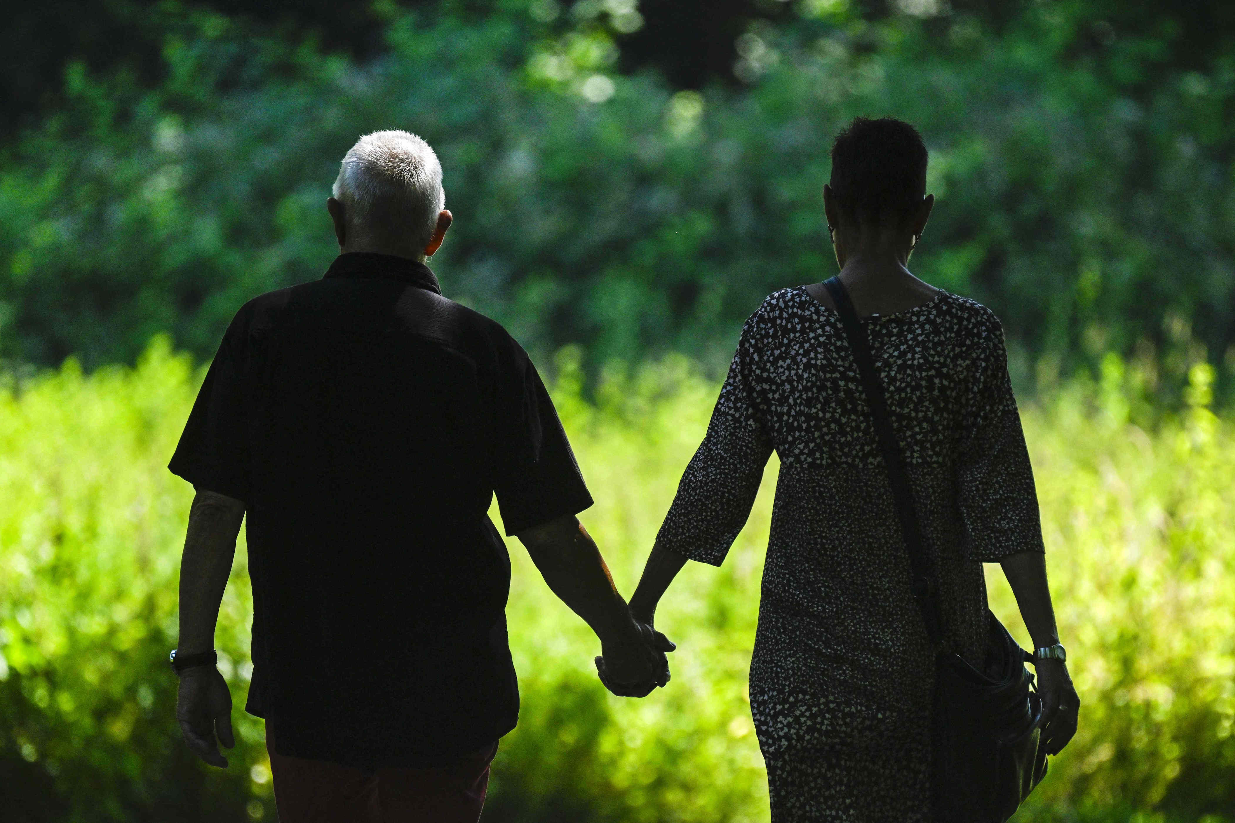 Two people holding hands while walking in a grassy outdoor setting