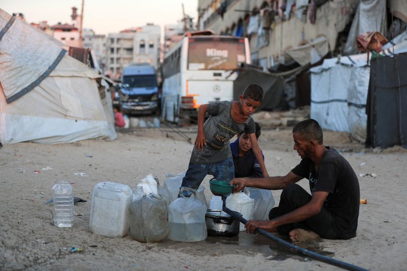 Displaced Palestinians fill water jerrycans at a tent camp sheltering displaced people, in Gaza