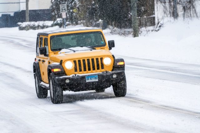 A vibrant yellow SUV navigates through a snowy urban street in winter conditions.