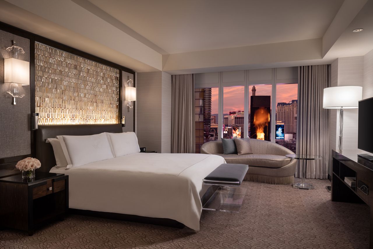 A luxury hotel room with a large bed seating area and a window providing a view of the skyline at sunset