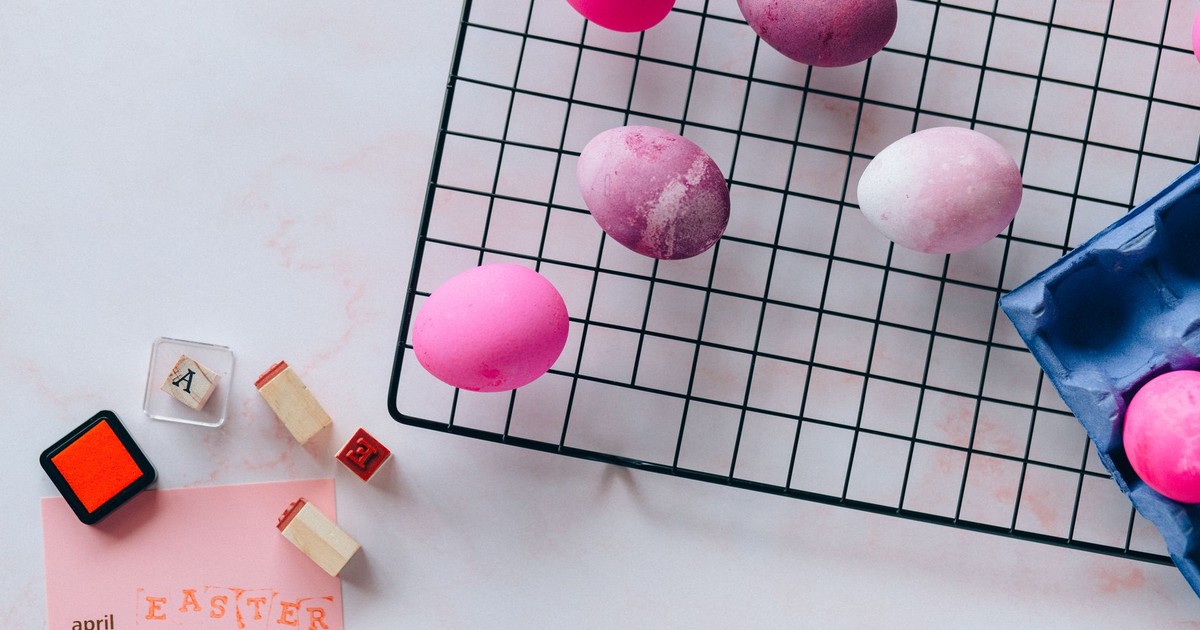 Flat lay of vibrant painted Easter eggs on drying rack with April calendar and stamp blocks.