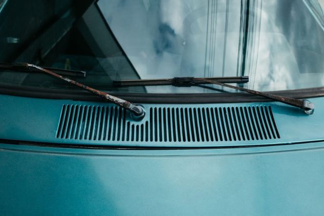 Close-up of rusty windshield wipers on a vintage car hood under a cloudy sky.