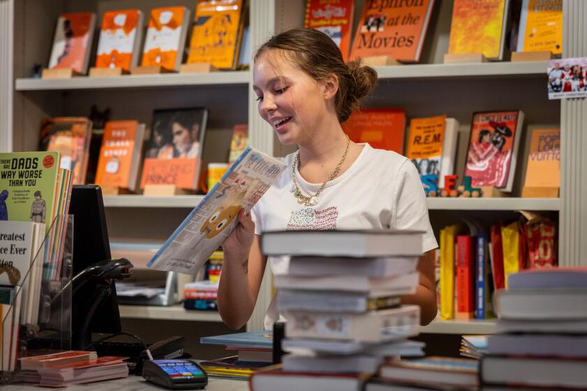A smiling young woman works at the checkout counter of a bookstore