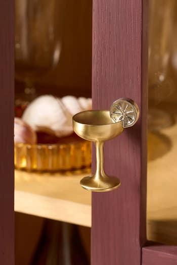 Gold champagne glass cabinet handle on a wooden surface, with blurred items in the background