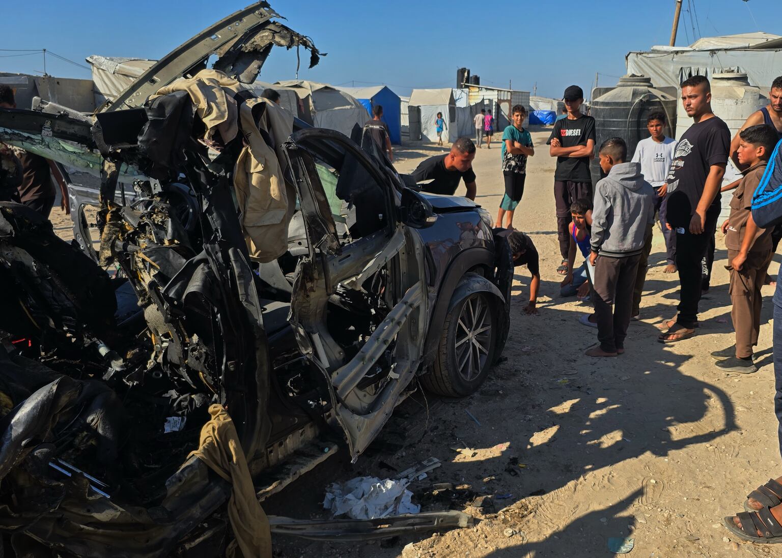 Palestinians look at a destroyed car following an Israeli military strike that, according to hospital officials, killed at least three people in Khan Younis, southern Gaza Strip (Mohammad Jahjouh/AP)
