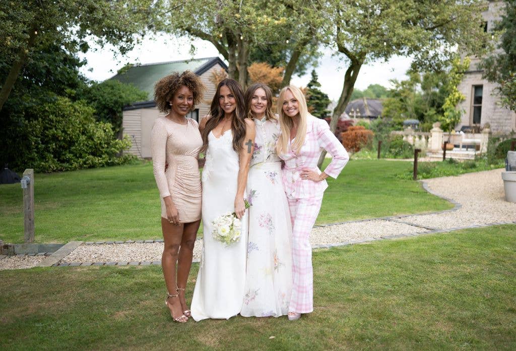 Four women, including Melanie C, Geri Halliwell, Emma Bunton, and Melanie Brown, stand together on a grassy lawn
