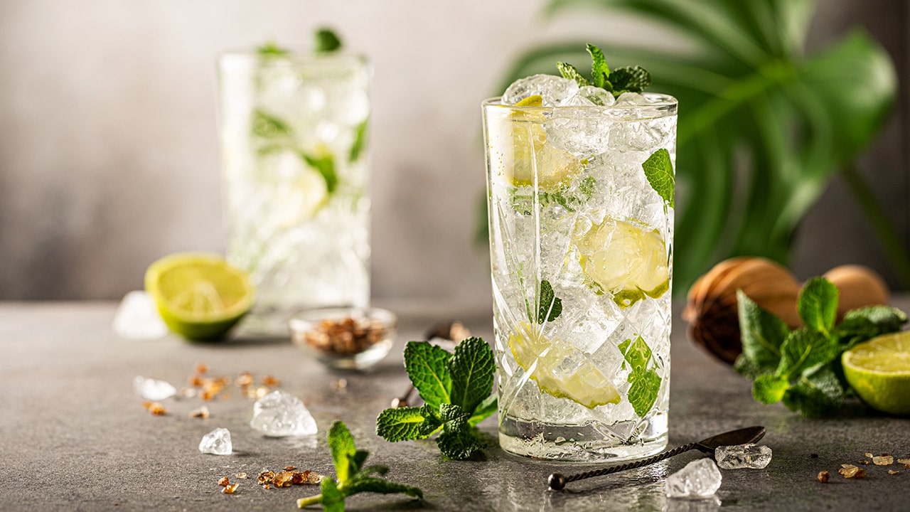A mojito is pictured in a glass with lime and mint, while another glass is shown out of focus in the background.