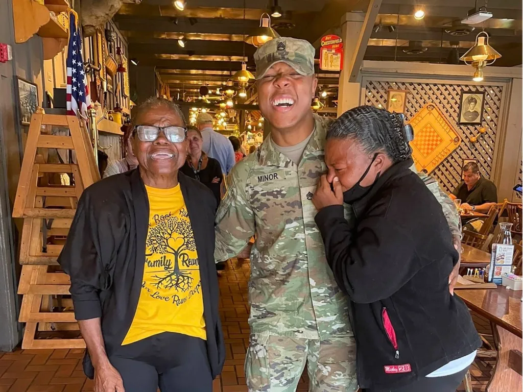 Soldier Emanuel smiles between veteran mom Laura and another emotional family member following his surprise homecoming.