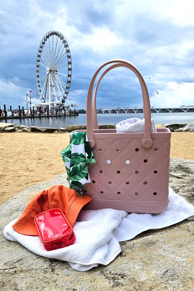 A tote bag with accessories lying on a towel a Ferris wheel visible in the background near a waterfront