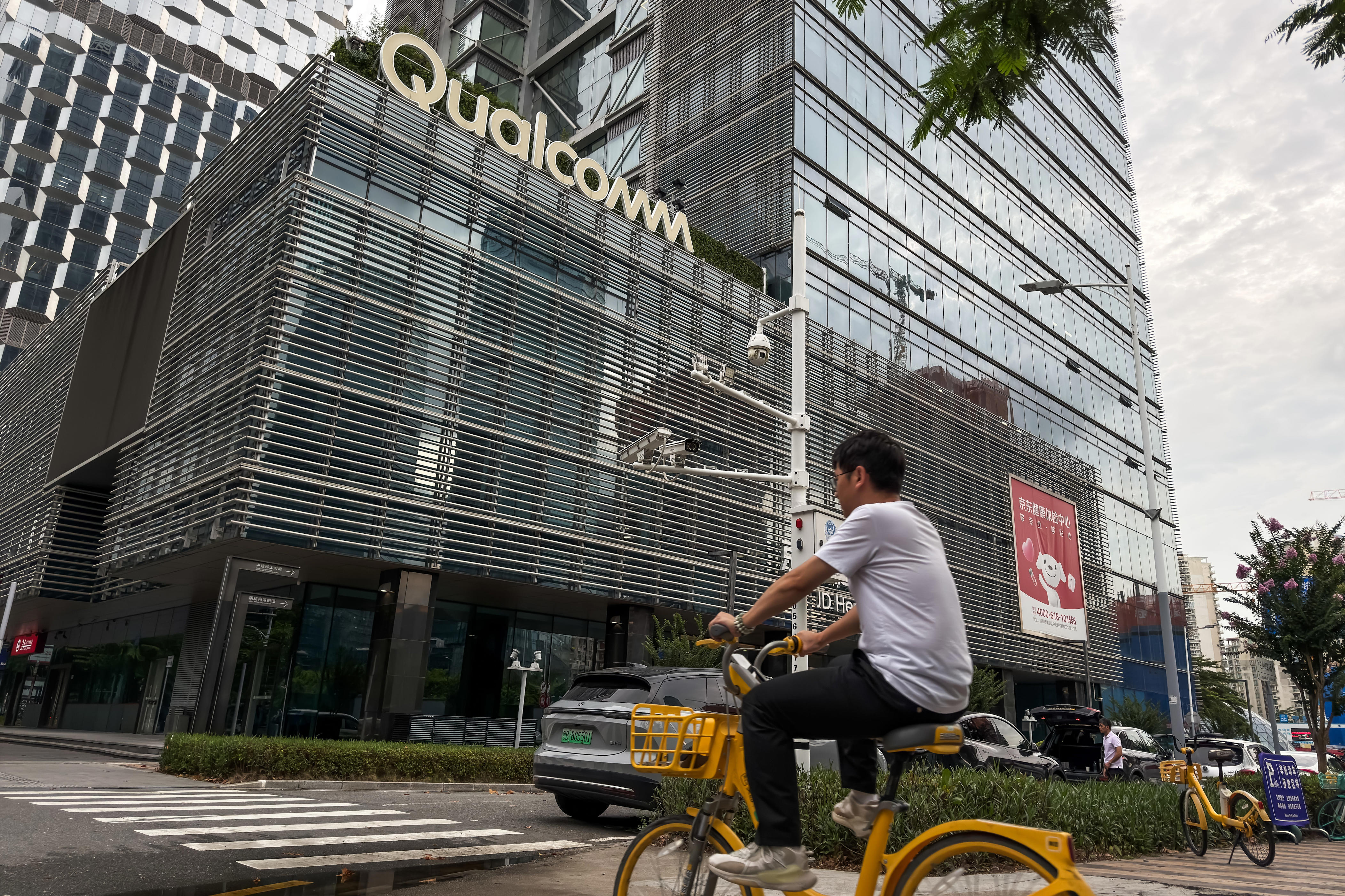 A cyclist rides past an office building bearing the Qualcomm logo
