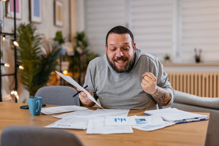 A person celebrates while looking through paperwork and seated at a table.