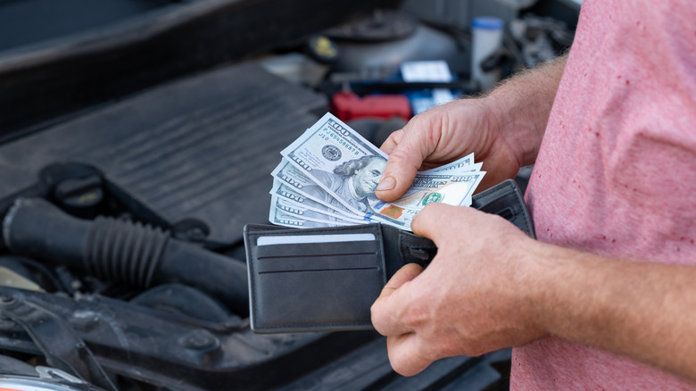 Customer taking dollar banknotes of his wallet to pay for car repair