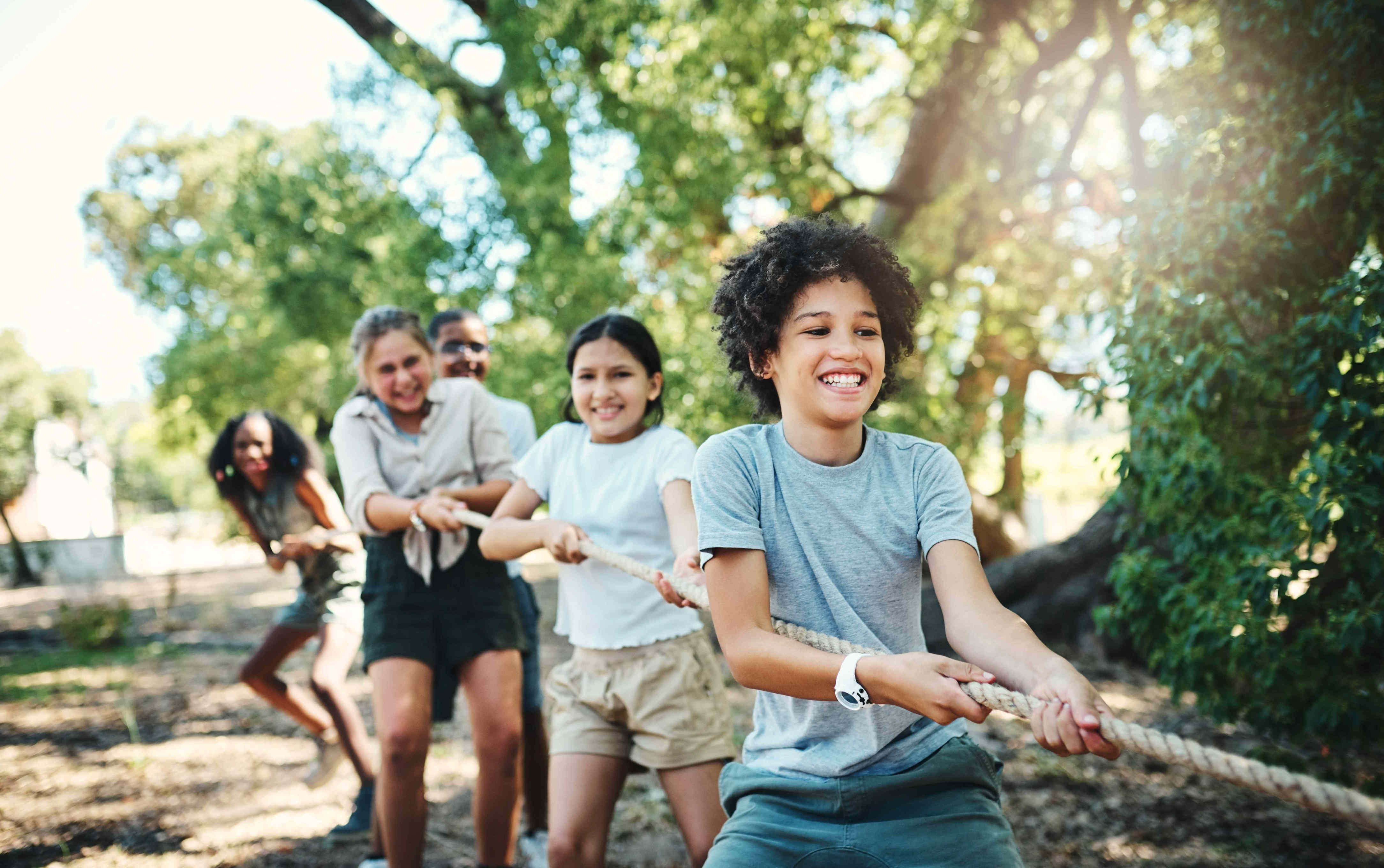 Children playing tugofwar outdoors at a summer camp smiling and pulling on the rope in a wooded area