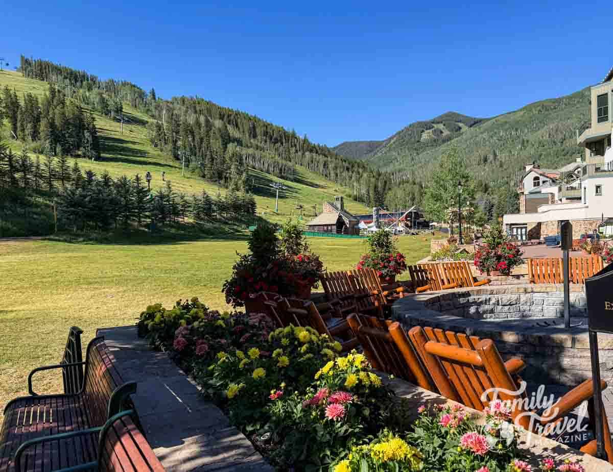 Lush summer view of Beaver Creek, Colorado, with green ski slopes, alpine village, and a flower-lined fire pit.