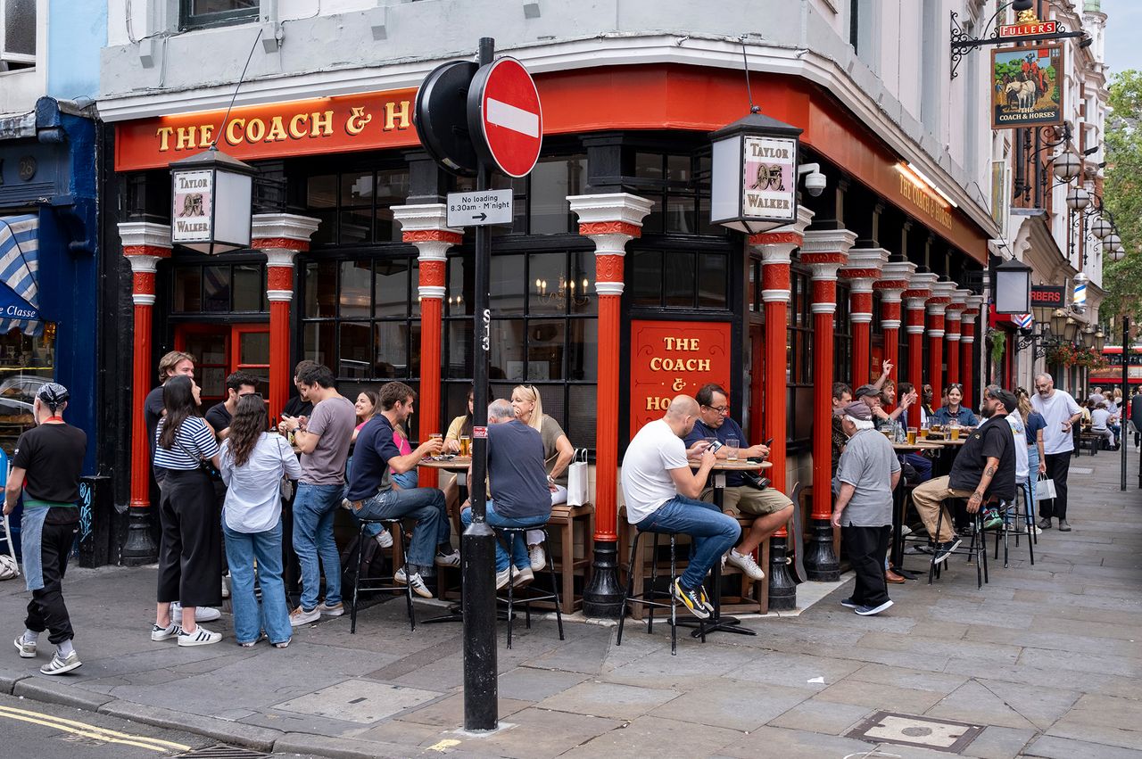 People seated and standing outside The Coach Horses pub on a city street corner