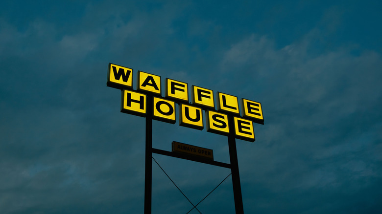 A yellow and black Waffle House sign against a dark sky.