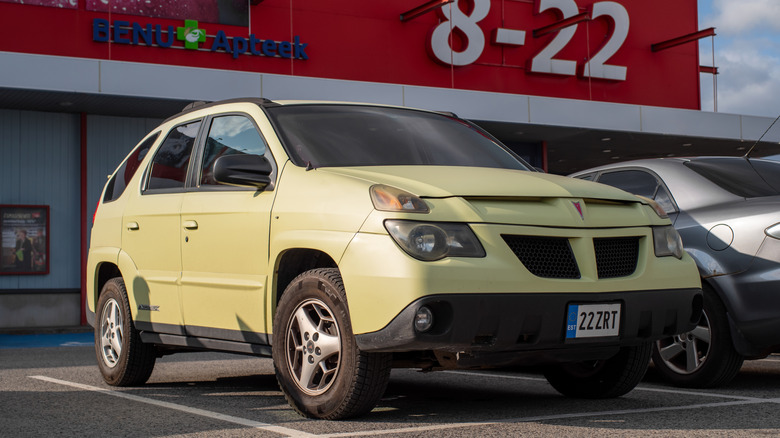Yellow Pontiac Aztek 2003 parked in front of a grocery store on a sunny summer evening.