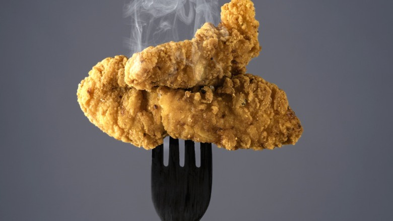 Chicken tenders on a fork, steaming against a grey background