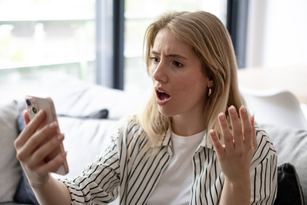 Woman appearing shocked while reading message on a mobile phone.