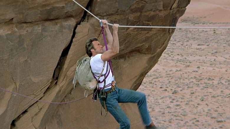 Clint Eastwood as Dr. Jonathan Hemlock in The Eiger Sanction, hand-over-hand traversing across a rope over a canyon.