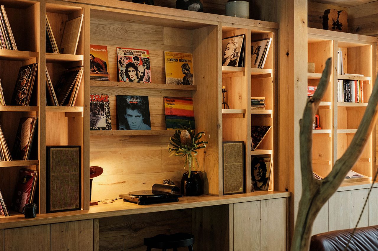 A set of wooden shelves containing vinyl records books and a record player in a cozy setting