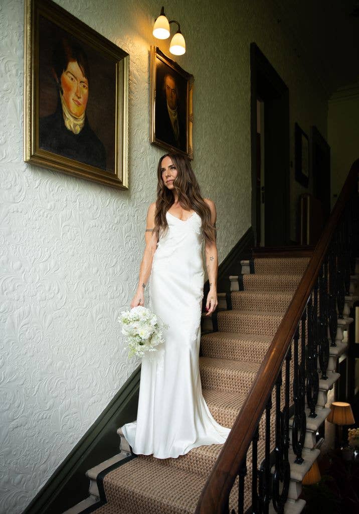 Melanie C stands on a staircase in a white gown holding a bouquet.