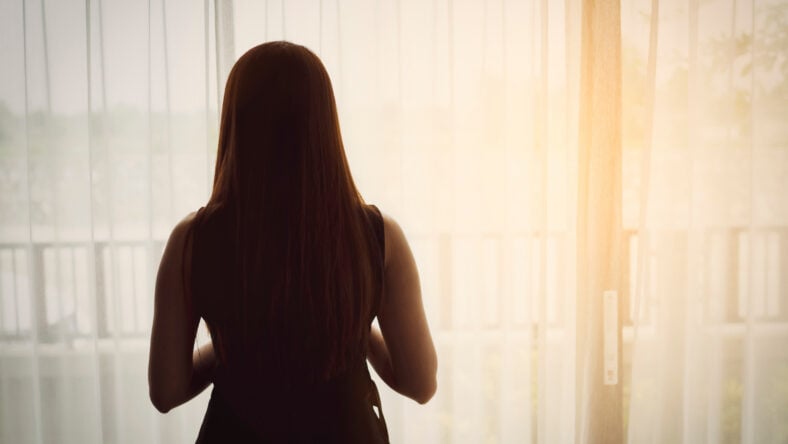 Back view of woman standing beside the windows with sunlight in the morning