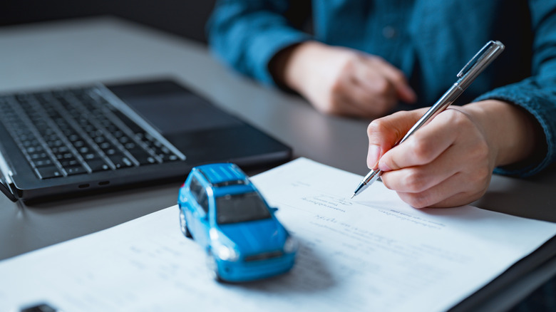 Person filling up a document with an SUV paperweight in the foreground
