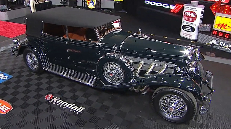 A black 1929 Duesenberg Model J Convertible sedan on the auction floor at a Mecum event in the early 2020s.