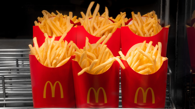 Six red, paper containers of McDonald's fries under the heat lamp