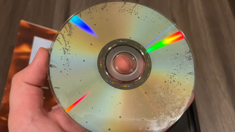 A hand holds up the backside of a reflective disc, where constellations of small pinpricks reveal that the CD has suffered from disc rot.