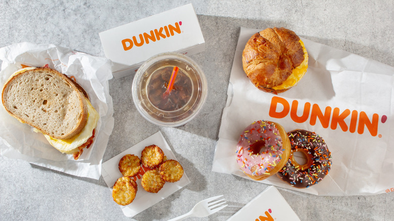 A top-down view of a Dunkin' spread, featuring an iced coffee, hash browns, a sandwich, a croissant, and two donuts.