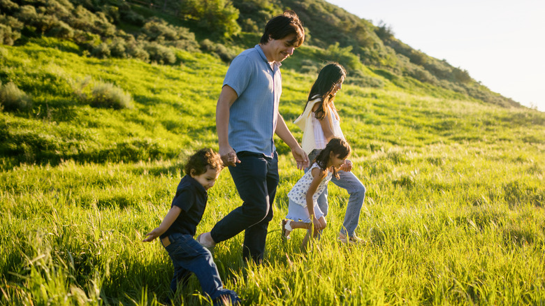 father, mother, and two kids walking in grassy area