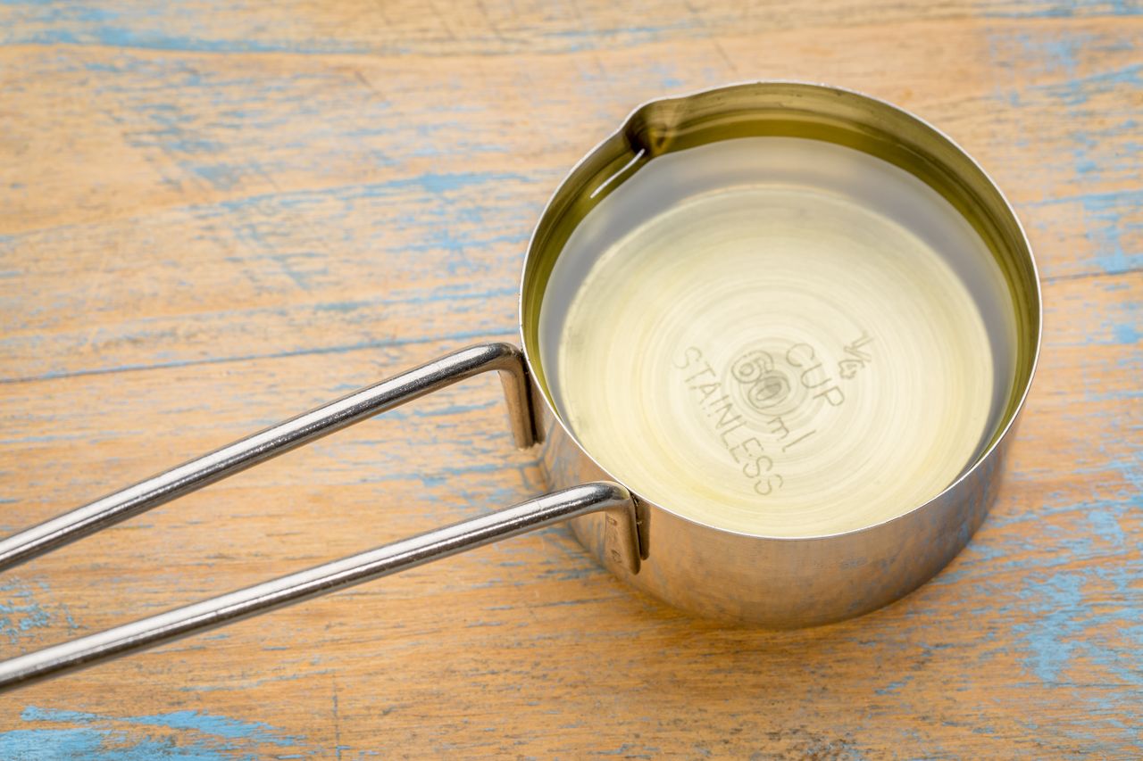 A stainless steel measuring cup filled with oil on a wooden surface