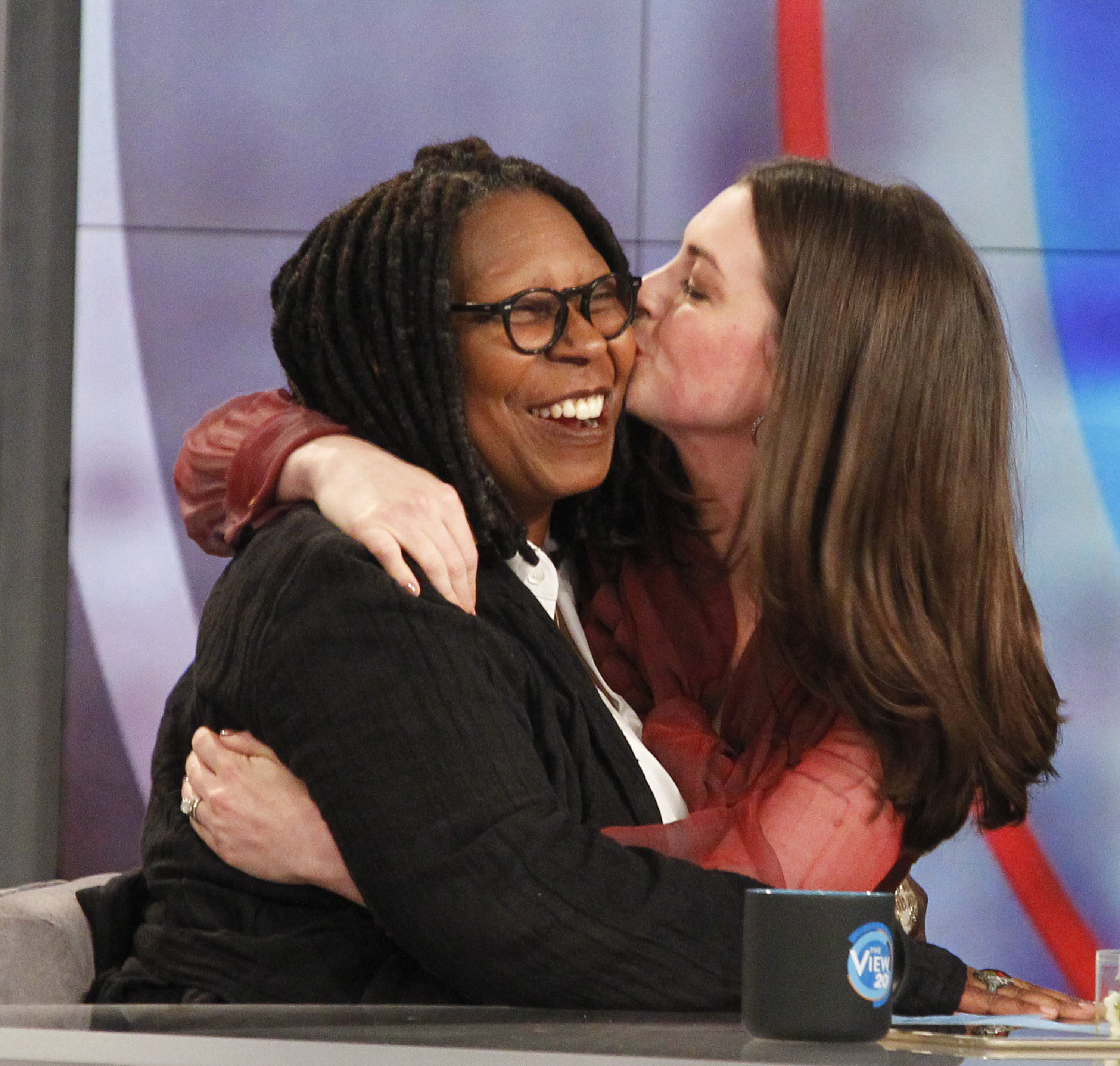 Anne Hathaway kissing Whoopi Goldberg on the cheek during an episode of 