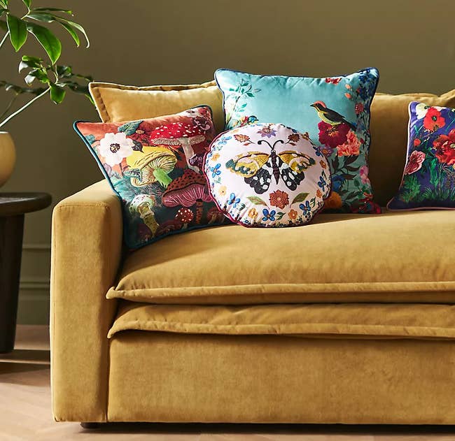 Decorative cushions with floral and nature patterns arranged on a mustard-colored sofa, enhancing a cozy living space