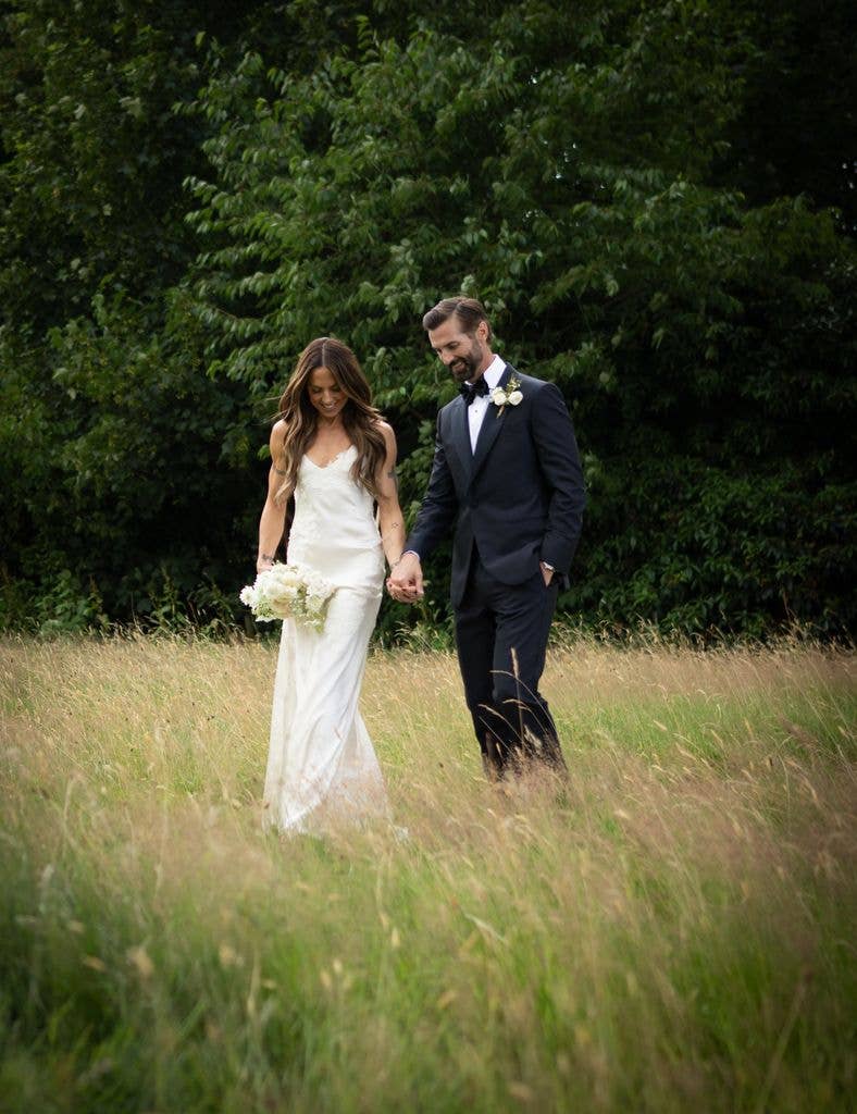 Melanie C and Chris Dingwall walk hand in hand through tall grass.