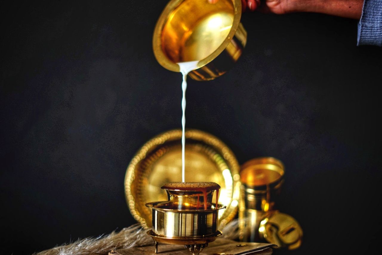 Traditional South Indian coffee preparation with milk being poured into a brass tumbler and filter