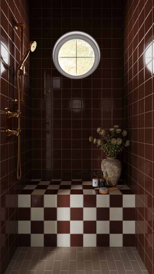 Bathroom with checkered tile floor red wall tiles circular window brass shower fixtures and a decorative vase on a ledge