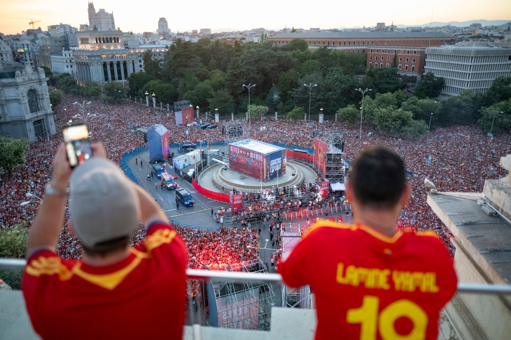 MADRID, SPAIN - 2026/07/20: An elevated view shows fans wearing Lamine Yamal national jerseys looking out over a massive crowd packed into Plaza de Cibeles around a stage displaying banners reading