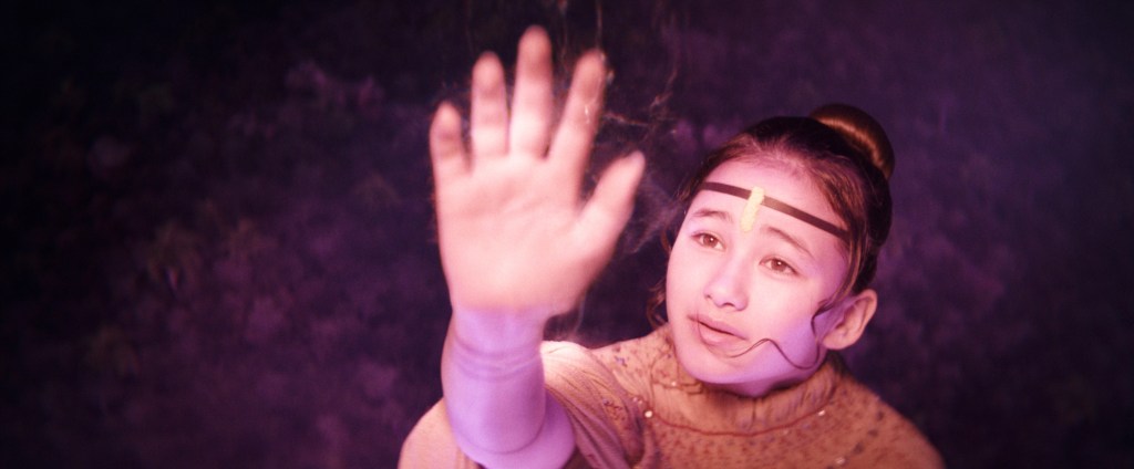 Kaylee Hottle as Jia, looking up with her hand raised.