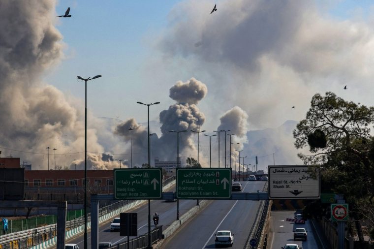 TOPSHOT - Motorists drive along an expressway as plumes of smoke rise after a strike in Tehran on March 5, 2026. Israel pounded Tehran with fresh strikes and Iran targeted Kurdish guerilla groups in Iraq on March 5 as a spiralling war in the Middle East engulfed the entire region. (Photo by ATTA KENARE / AFP via Getty Images)