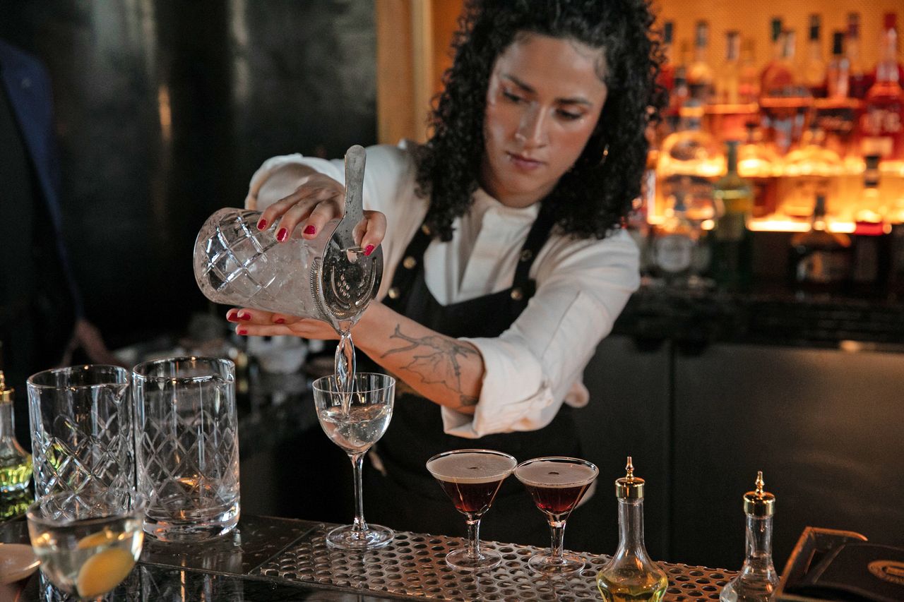 A bartender pouring a drink into a glass at a bar