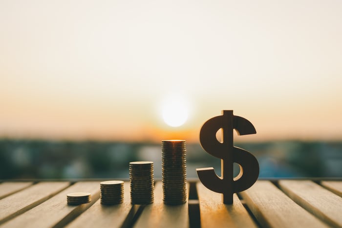 Rising bars and a dollar sign in front of a sunset.