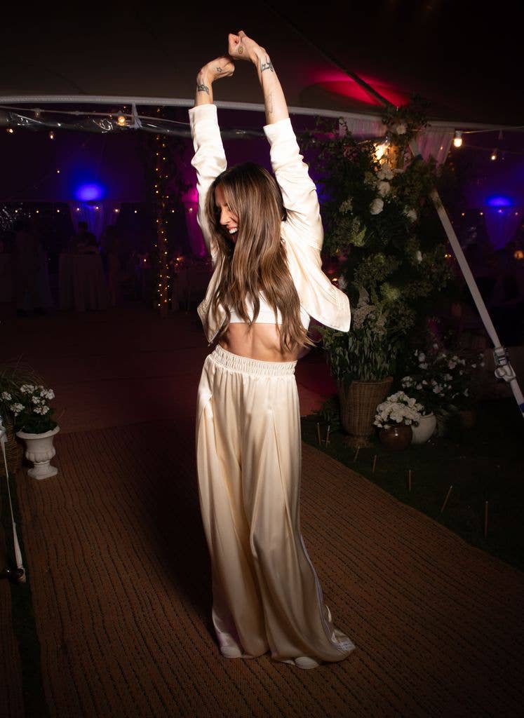 Melanie C in a white satin outfit dances with her arms raised at a party.