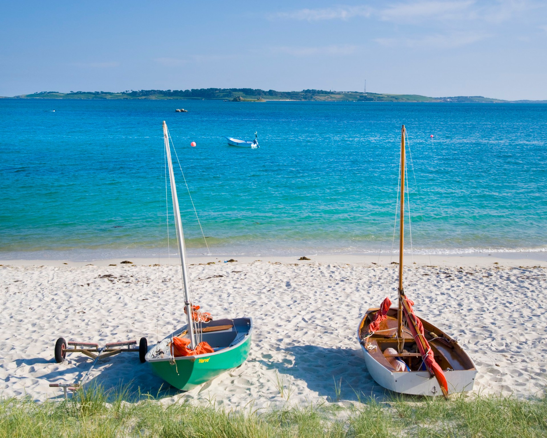 Two lone boats sitting on the white sand of St. Martins Beach, on the Isles of Scilly. There is turquoise and blue sea behind the sand.