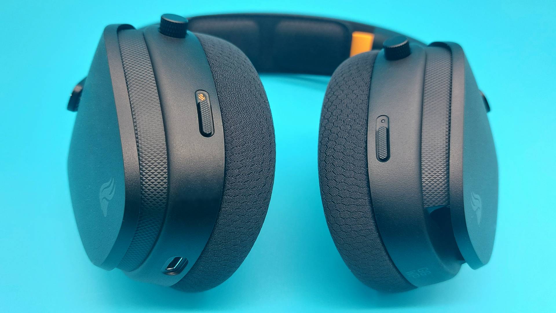 The GHS Wireless InfinitePlay seen from various angles on a blue background. This is a wireless gaming headset from Glorious. It is black all over, save for a few subtle orange accents.